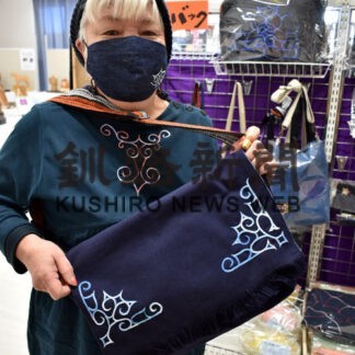 前垂れを改造し、アイヌ文様を縫い付けたバッグを手に越野さん
